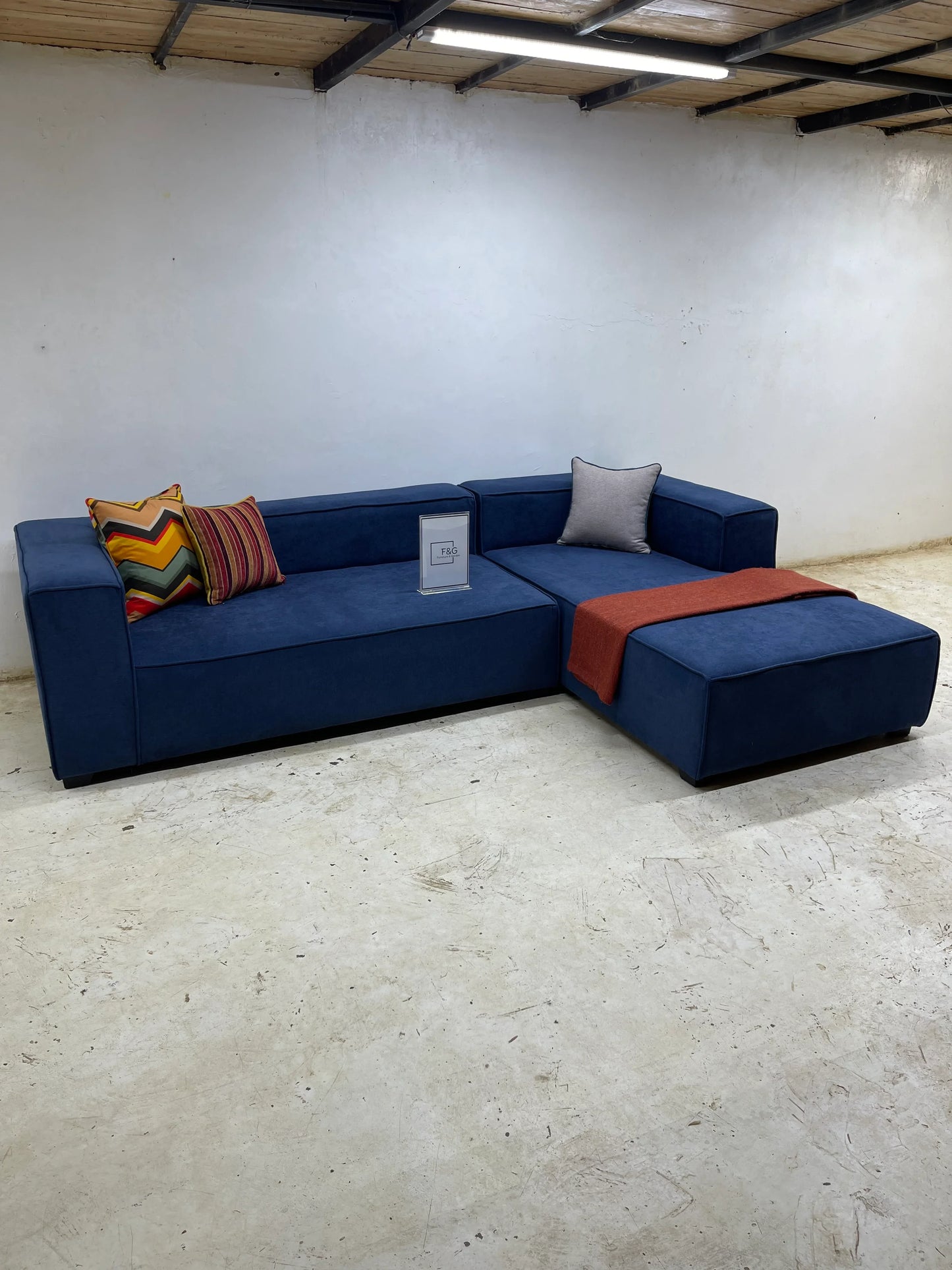 Modern navy blue sectional sofa with colorful and gray cushions, red throw in minimalist room