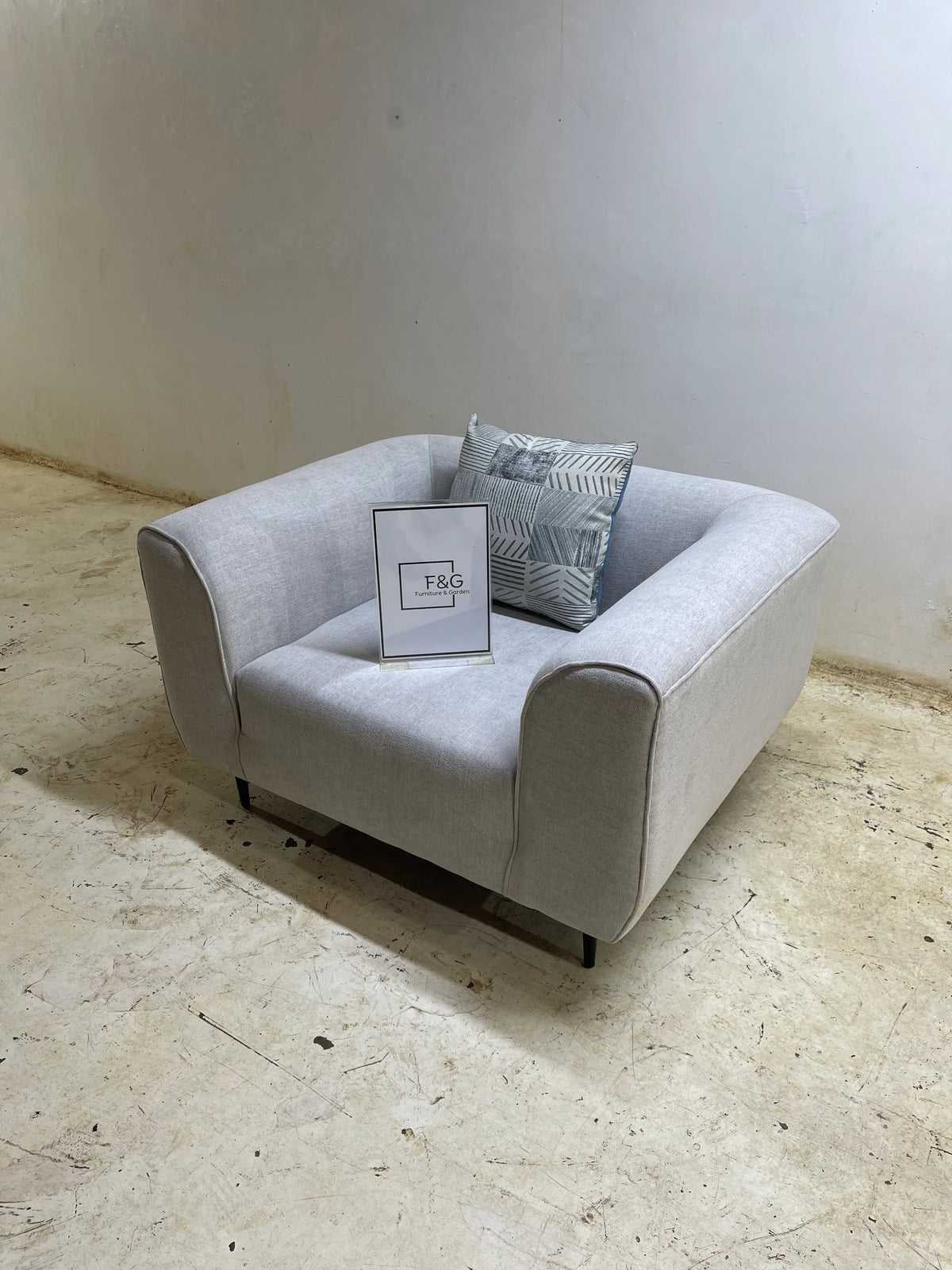 Modern light gray upholstered armchair with patterned cushion on textured concrete floor