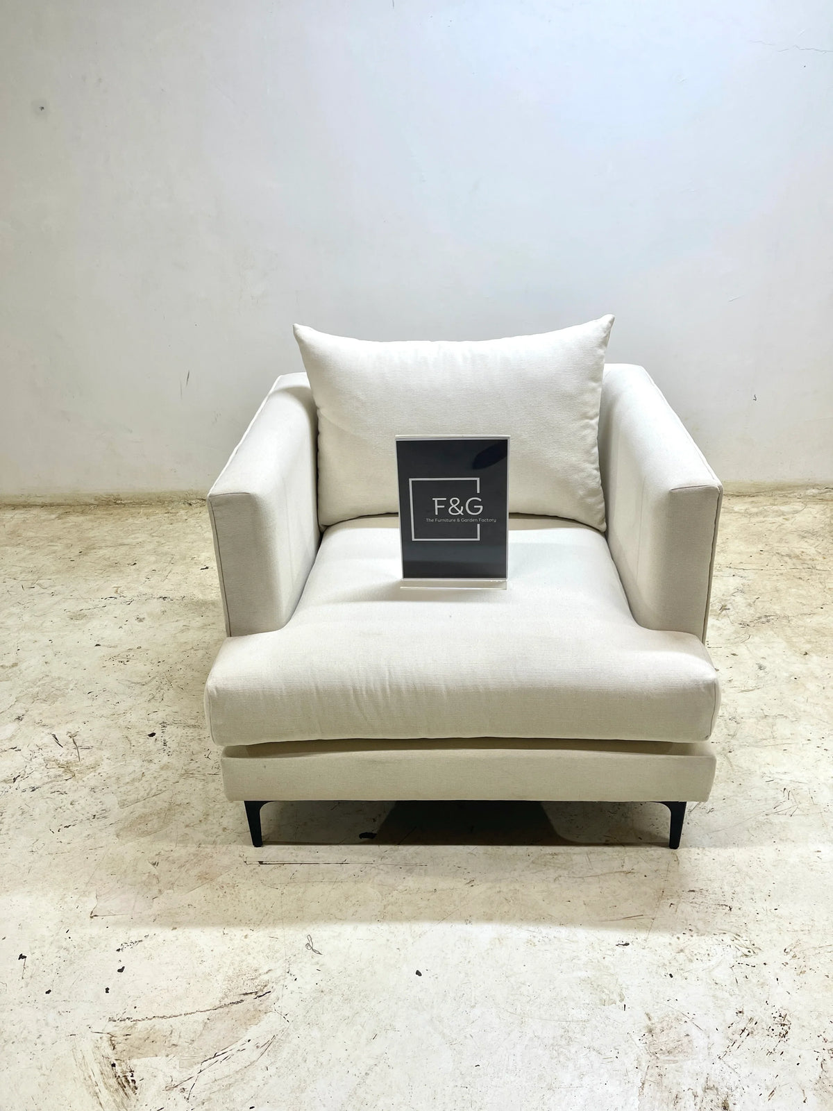 Modern beige armchair with cushion on textured beige floor and F&G sign on seat