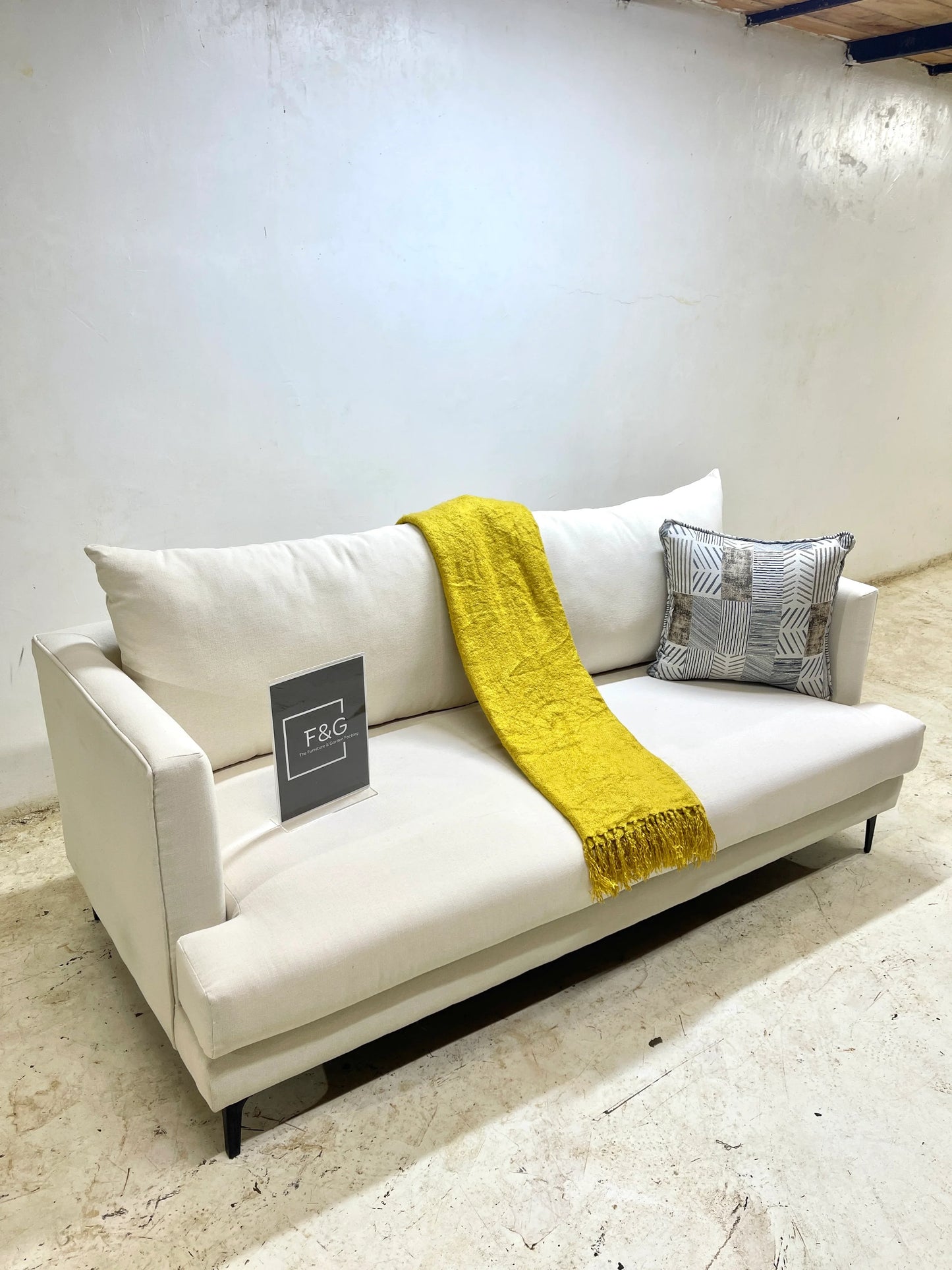 Modern white fabric sofa with black legs, mustard yellow throw, and patterned cushion in minimal room