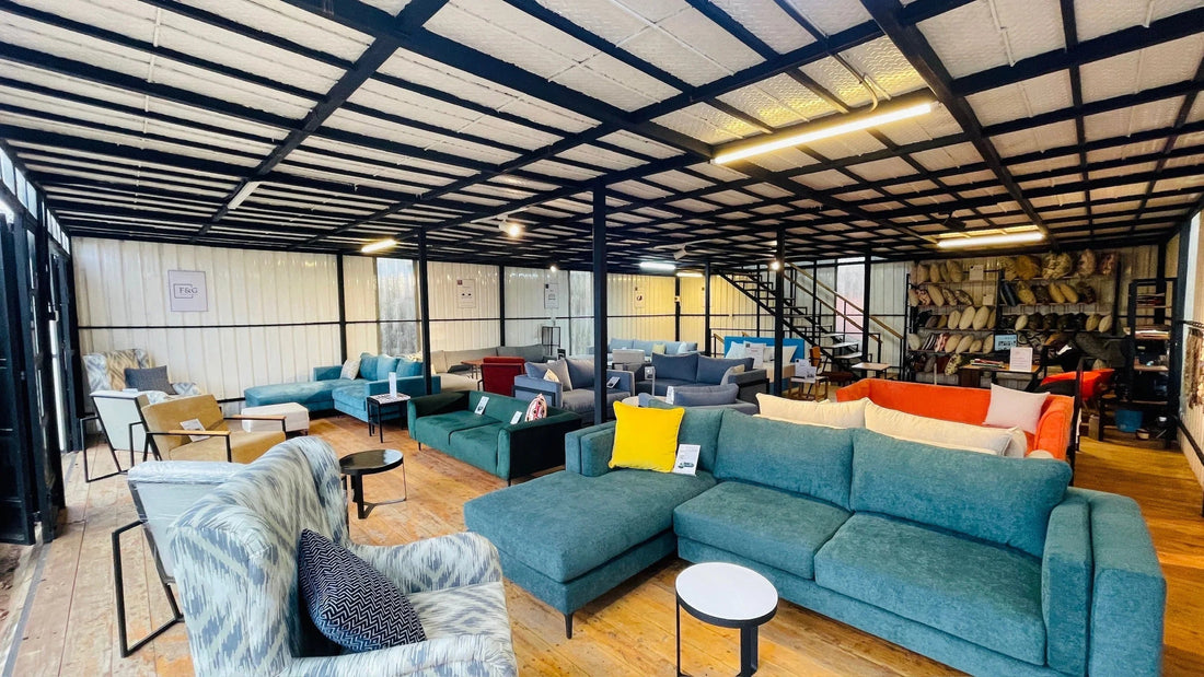 Modern furniture showroom with various sofas, armchairs, coffee tables, and shelves of pillows in an industrial-style space