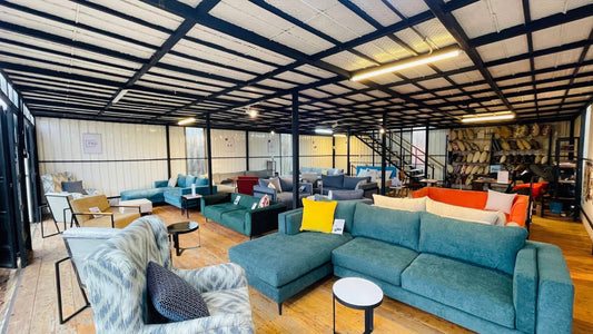 Modern furniture showroom with various sofas, armchairs, coffee tables, and shelves of pillows in an industrial-style space