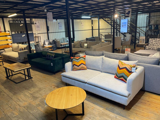 Modern furniture showroom with various sofas, colorful throw pillows, and wooden coffee tables on wooden floor