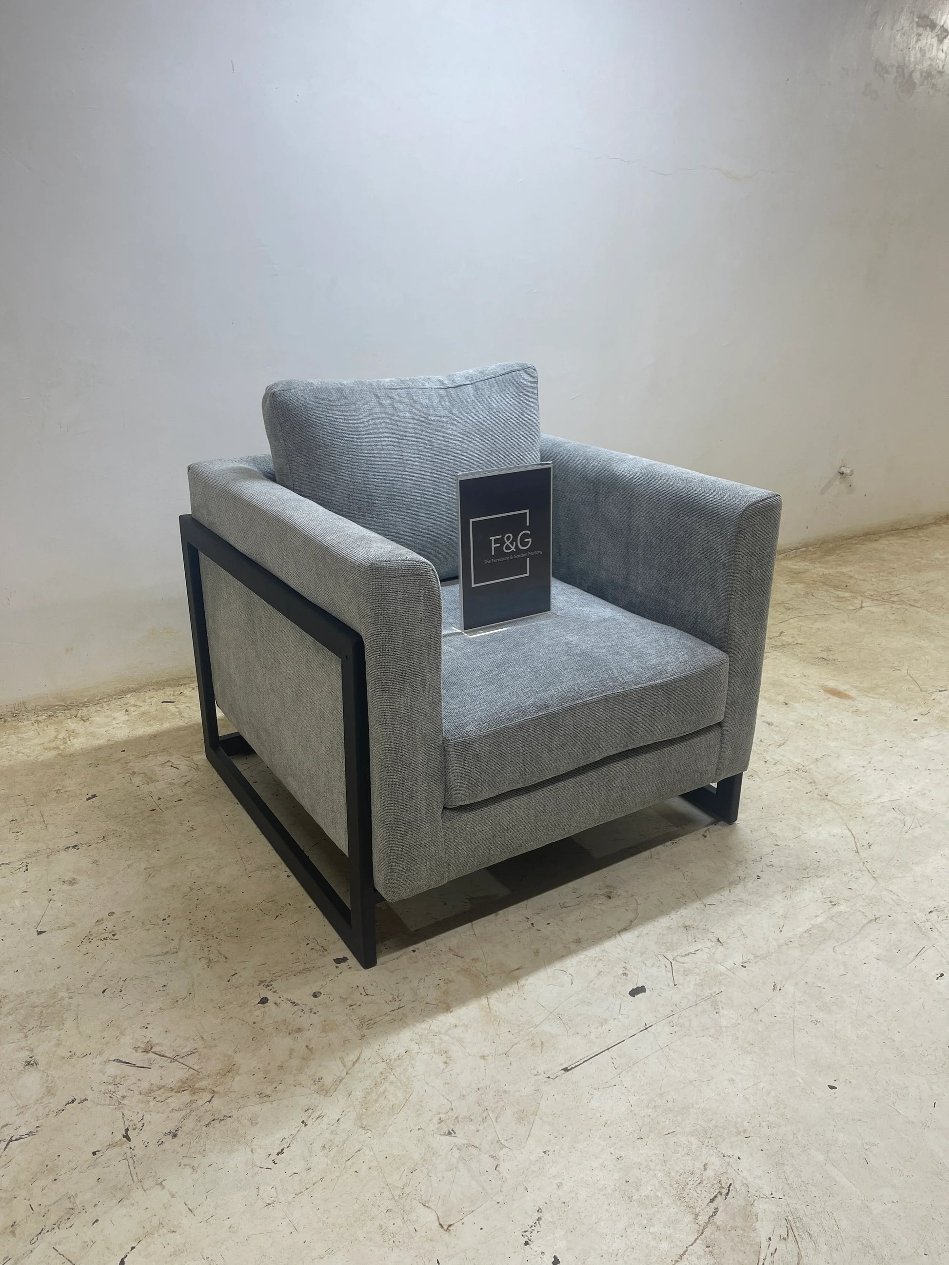 Modern gray fabric armchair with black metal frame on concrete floor against white wall