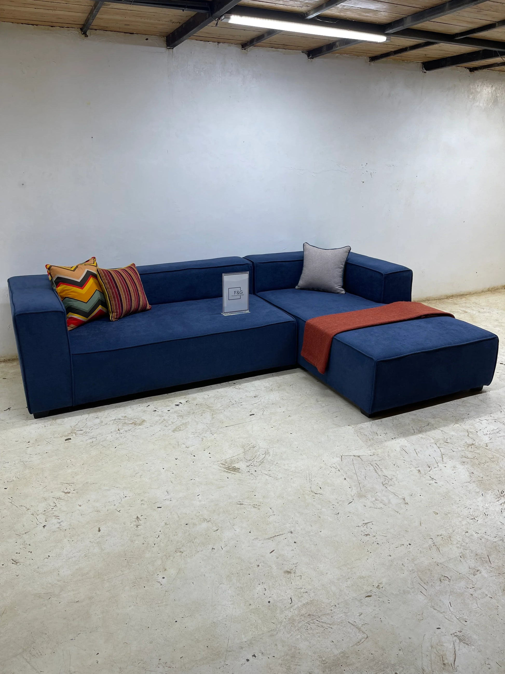 Modern navy blue sectional sofa with colorful and gray cushions, red throw in minimalist room