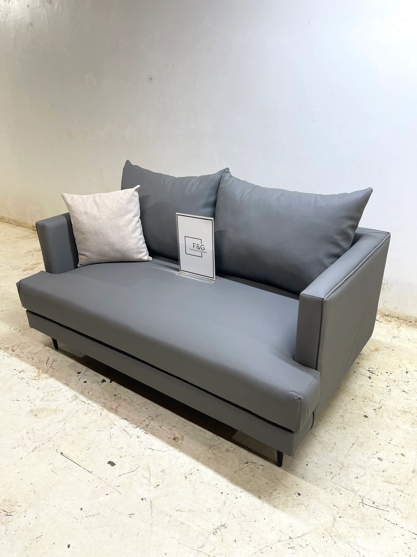 Modern gray leather sofa with two cushions on a light concrete floor against plain white wall