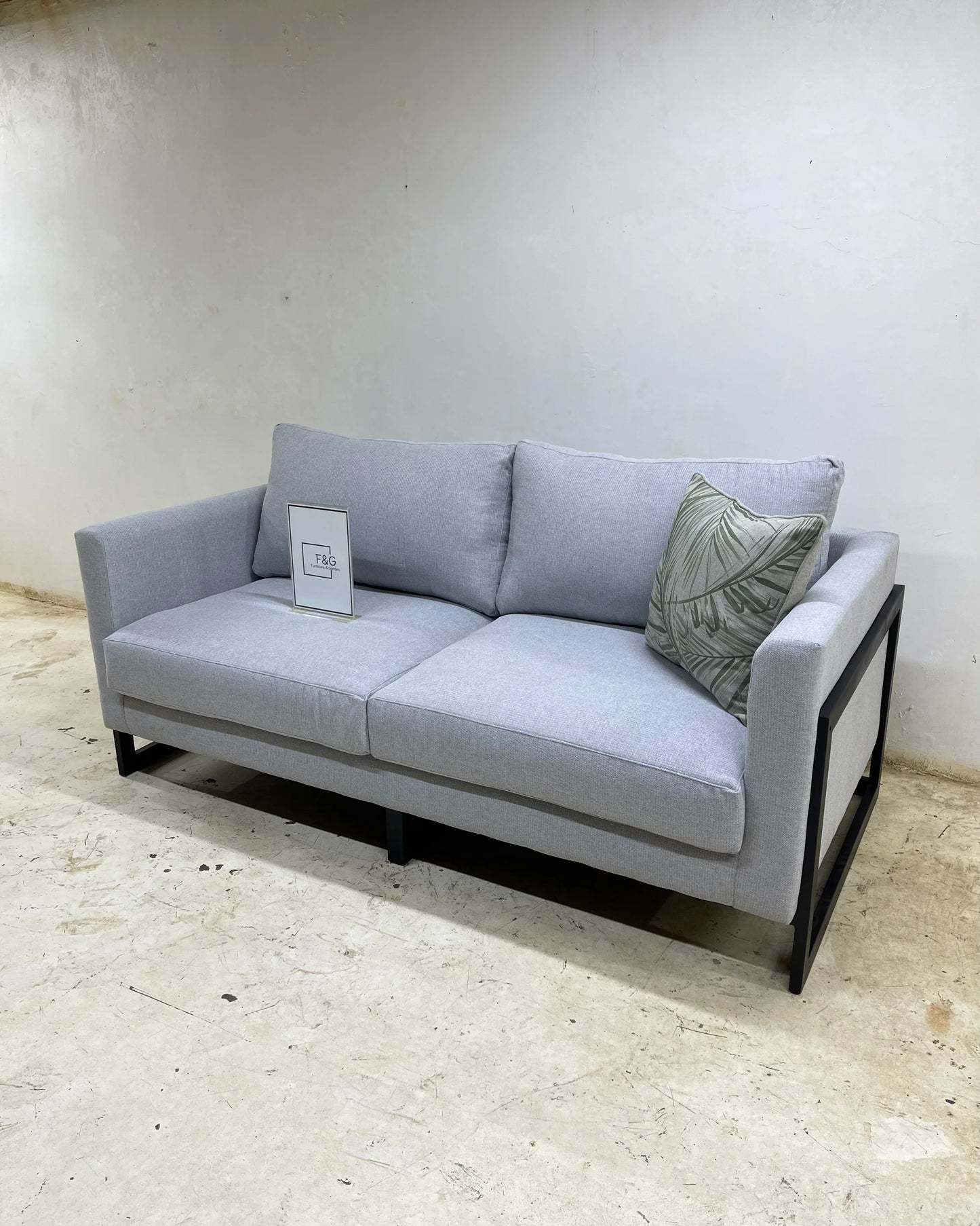 Modern light gray fabric sofa with black metal frame and a green leaf-patterned cushion