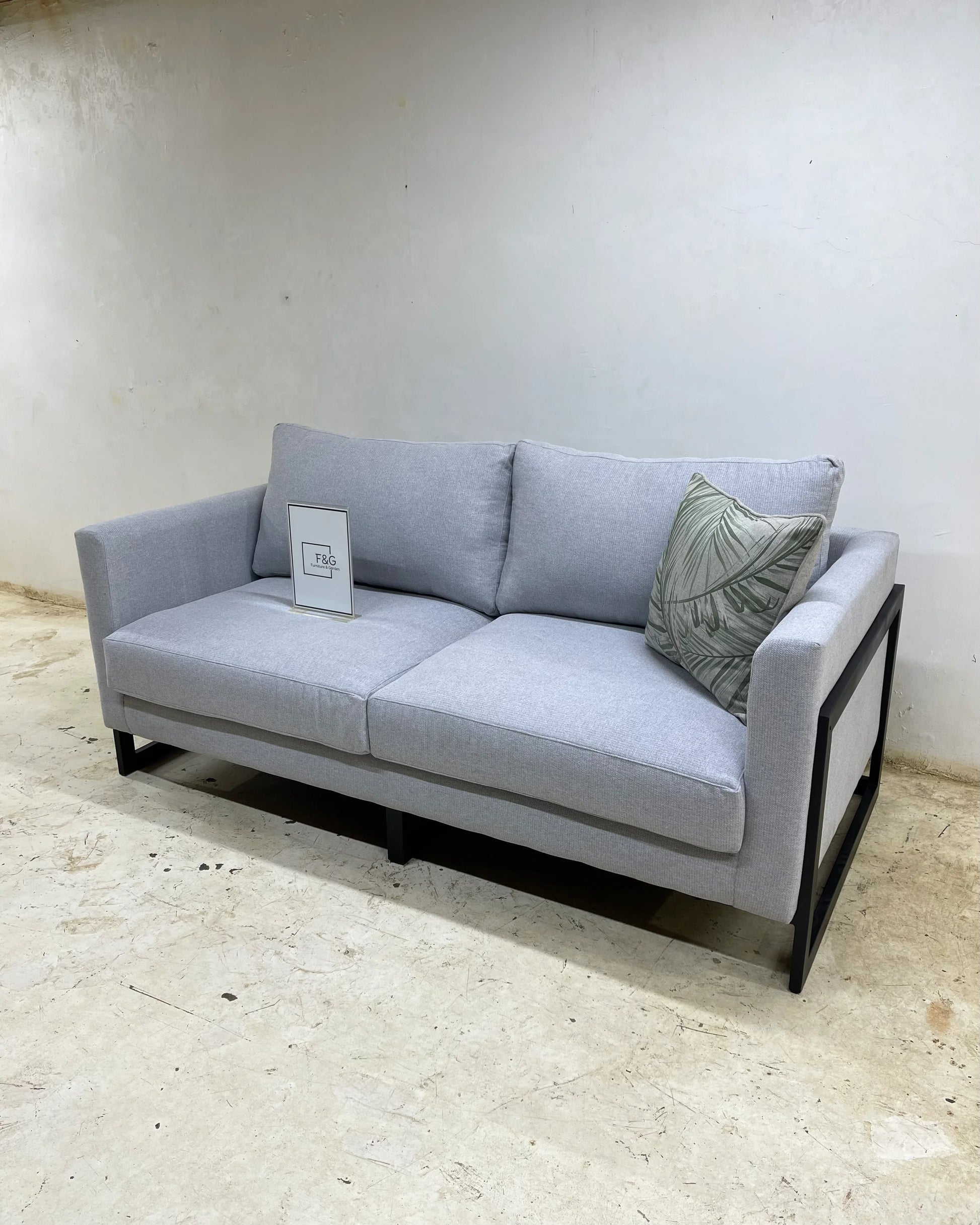 Modern light gray fabric sofa with black metal frame and a green leaf-patterned cushion