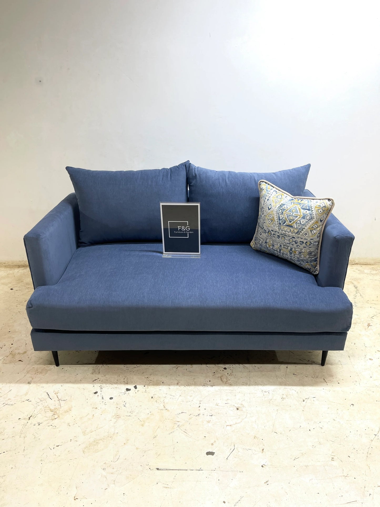 Modern blue fabric sofa with two solid cushions and one patterned accent pillow on concrete floor