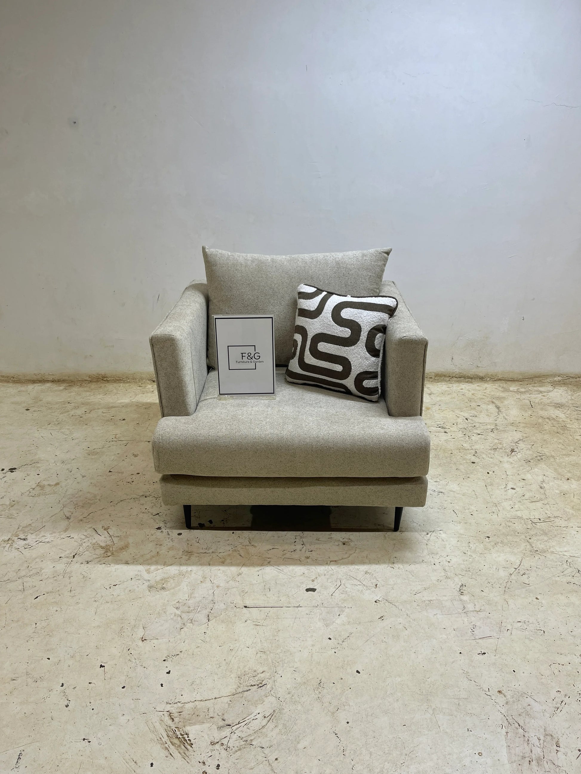 Modern beige armchair with patterned cushion and F&G Furniture & Garden sign on concrete floor
