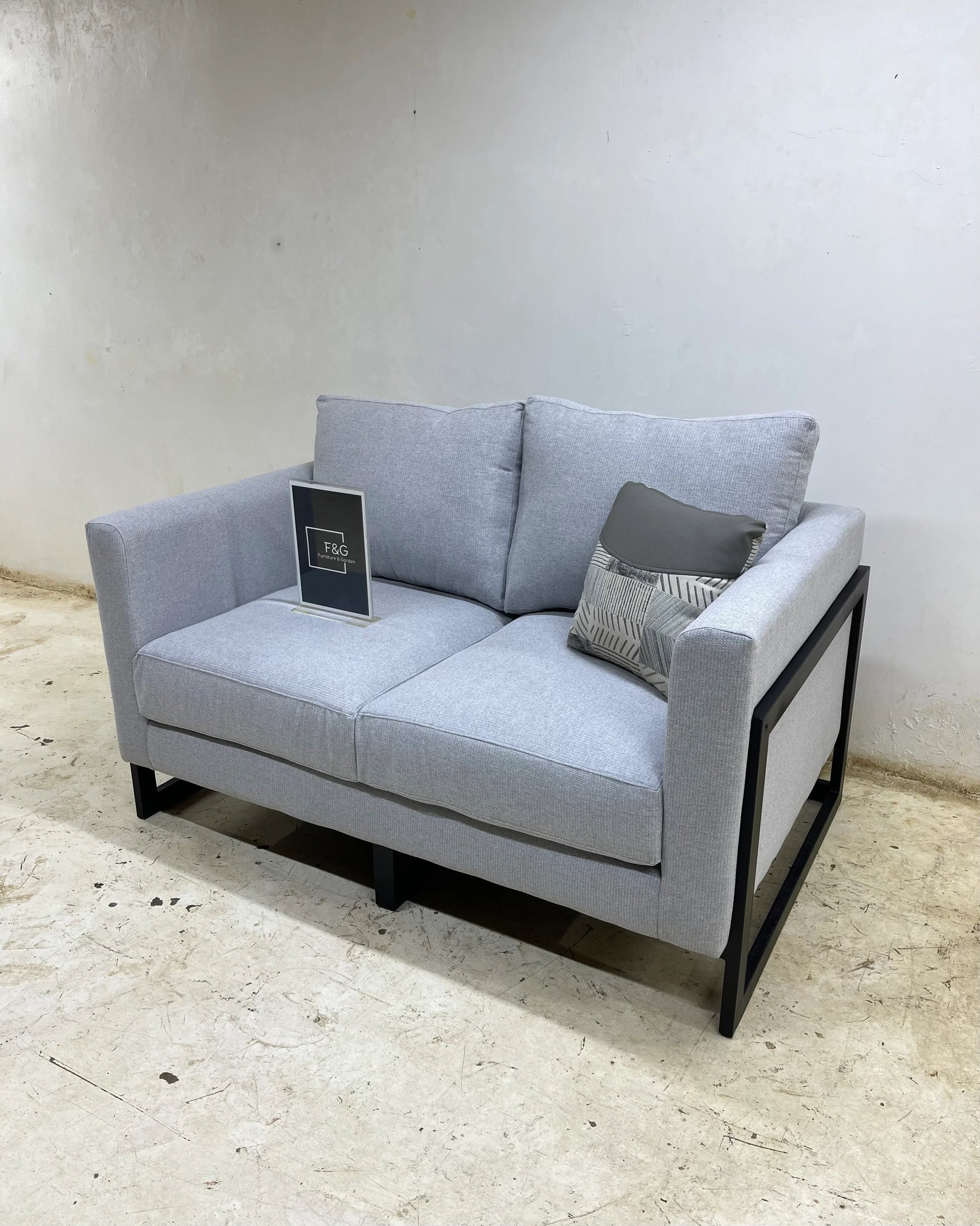 Modern light gray two-seater sofa with black metal frame and decorative pillow in minimalist room