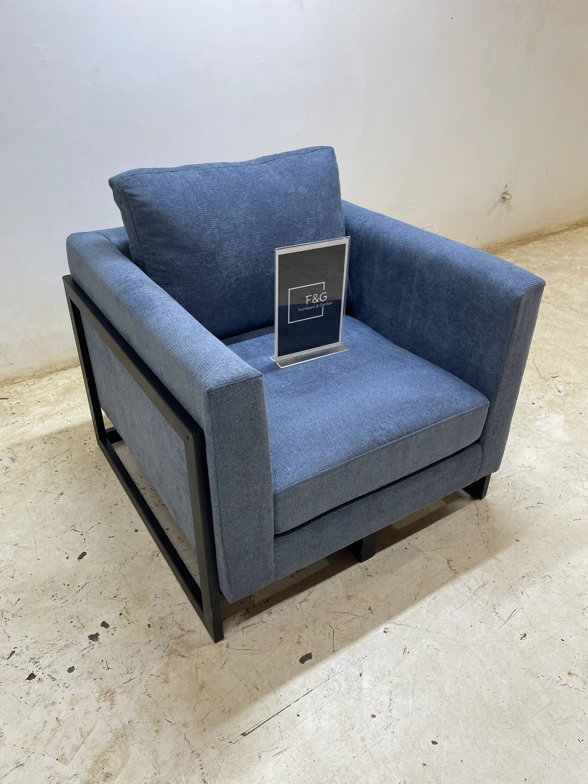 Blue upholstered armchair with black metal frame on beige floor against plain wall