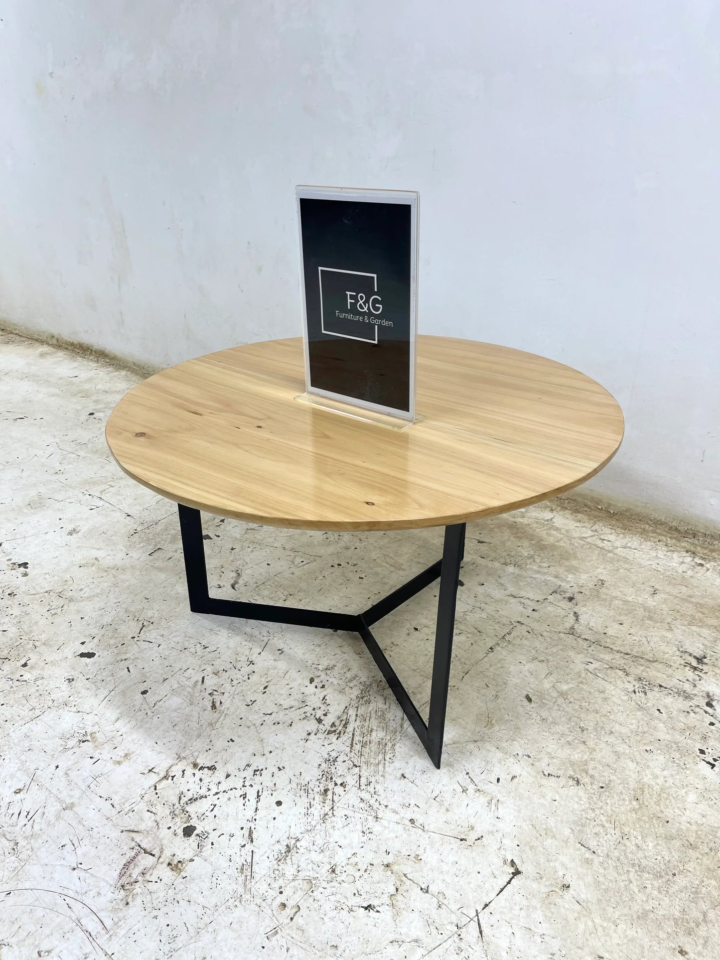 Round wooden coffee table with black metal legs on a distressed concrete floor indoors