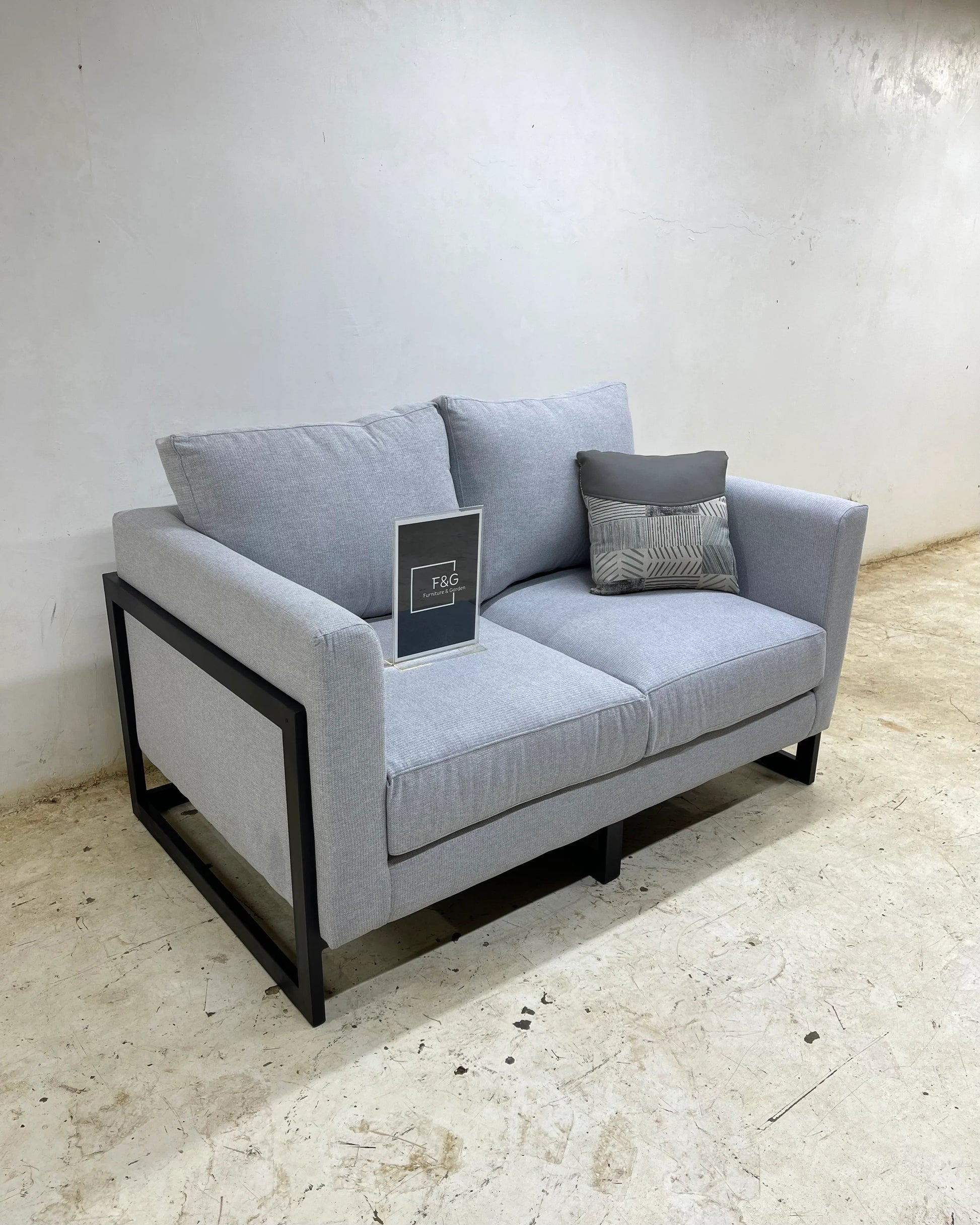 Modern gray fabric loveseat sofa with black metal frame and patterned cushion on concrete floor