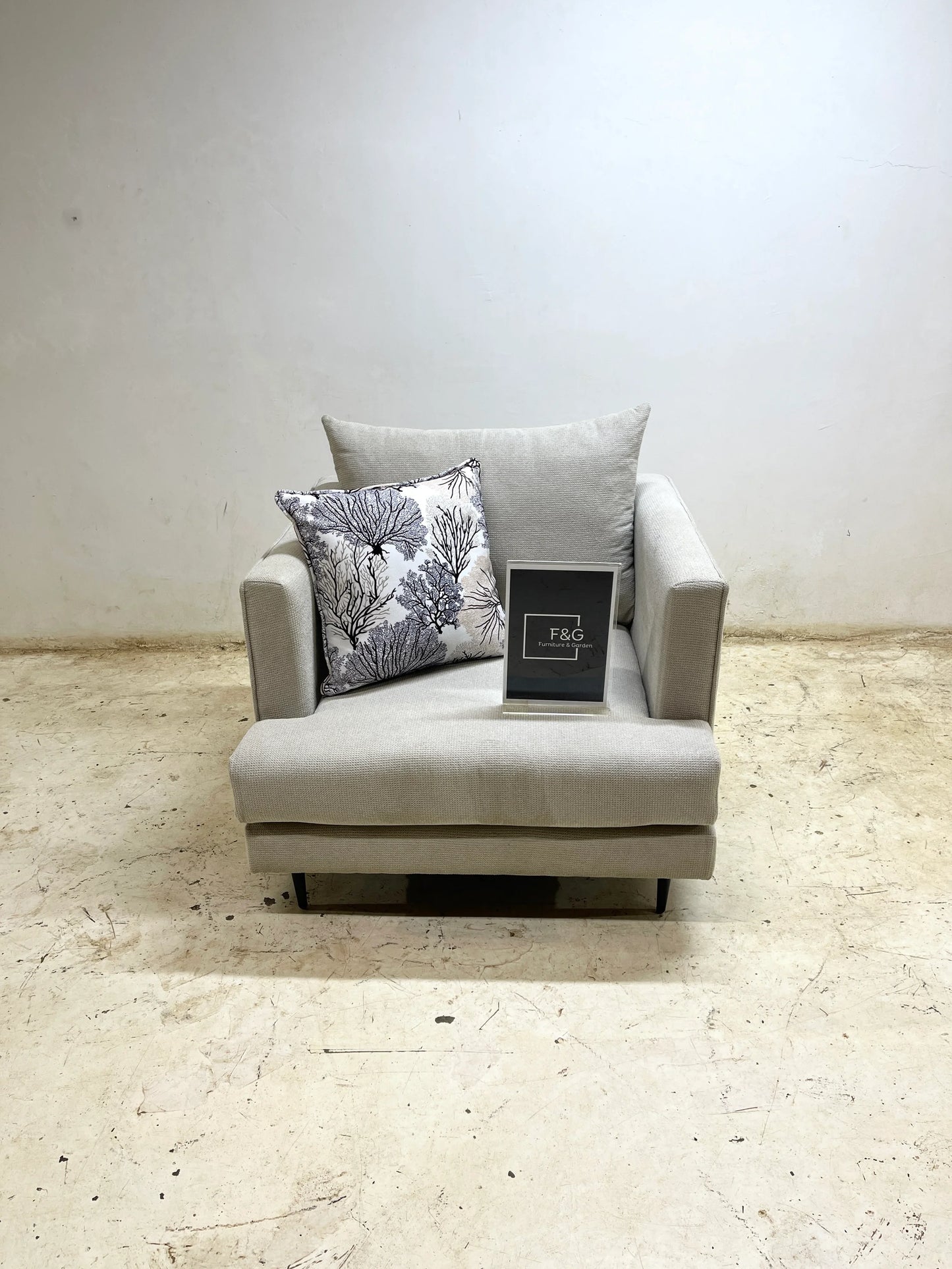 Light gray fabric armchair with decorative coral print pillow and F&G Furniture & Garden sign