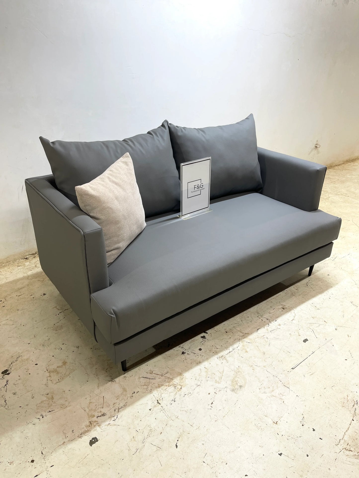 Modern grey fabric two-seater sofa with two dark grey cushions and one beige cushion on textured floor