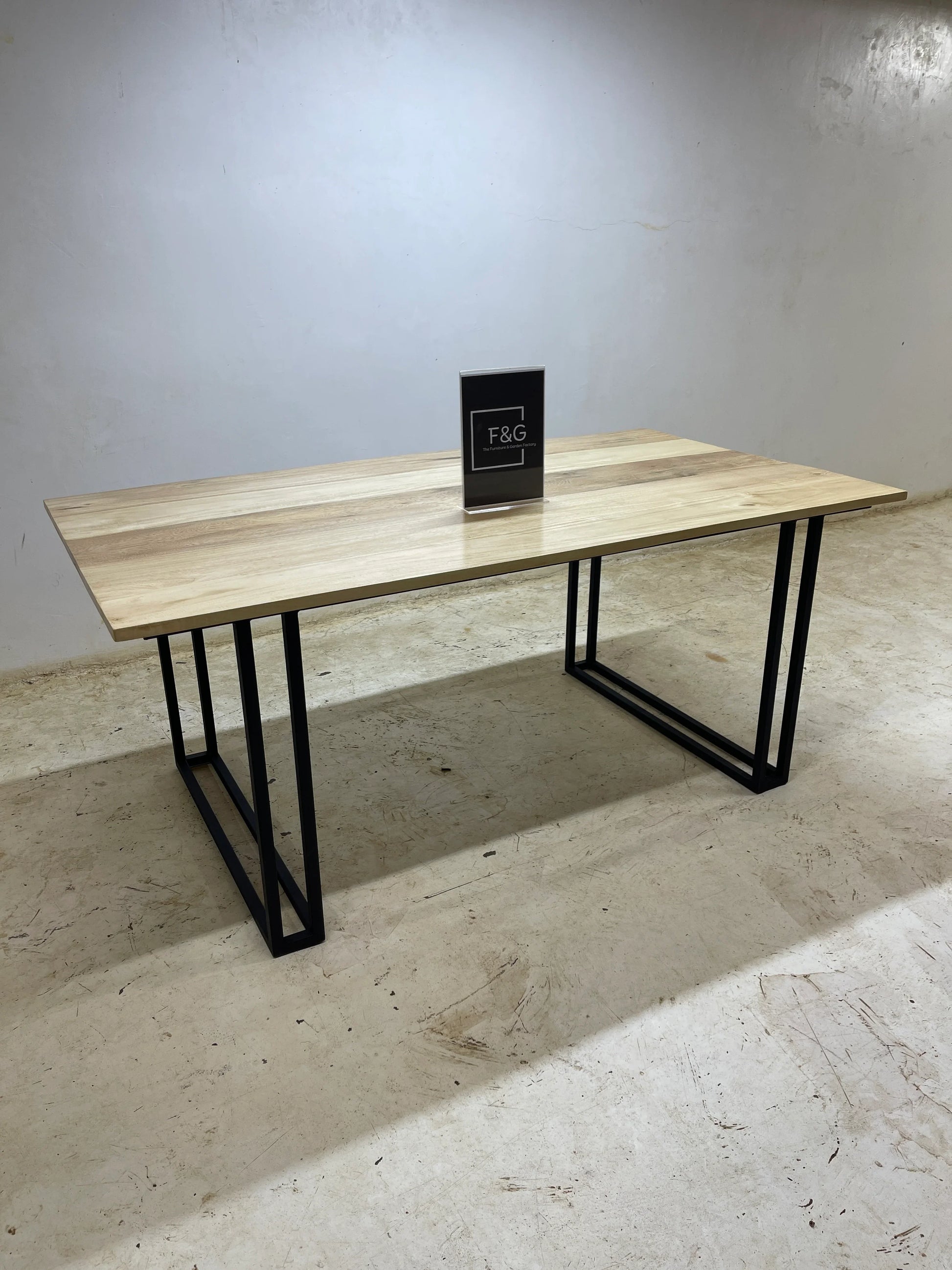 Modern wooden table with black metal legs on a concrete floor against a plain wall