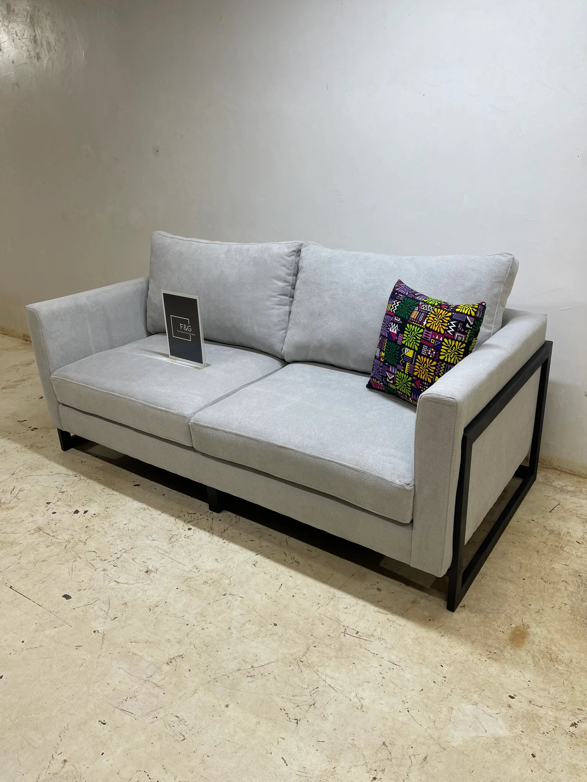 Modern light gray fabric sofa with black metal frame and colorful patterned cushion on concrete floor