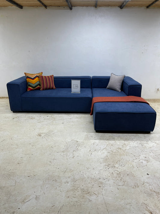 Modern blue L-shaped sofa with colorful and gray cushions and an orange throw in minimal room