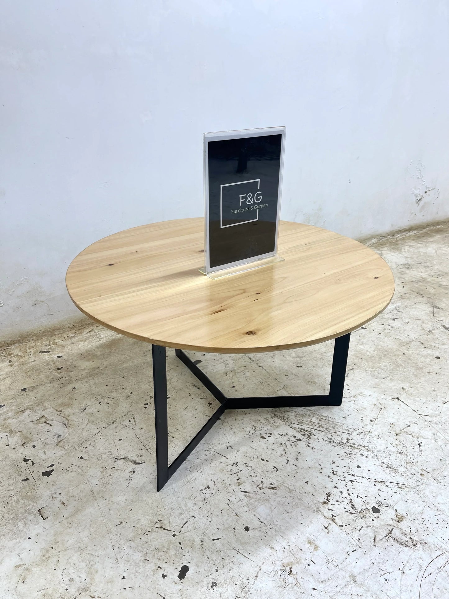 Modern round wooden coffee table with black metal tripod legs on textured concrete floor