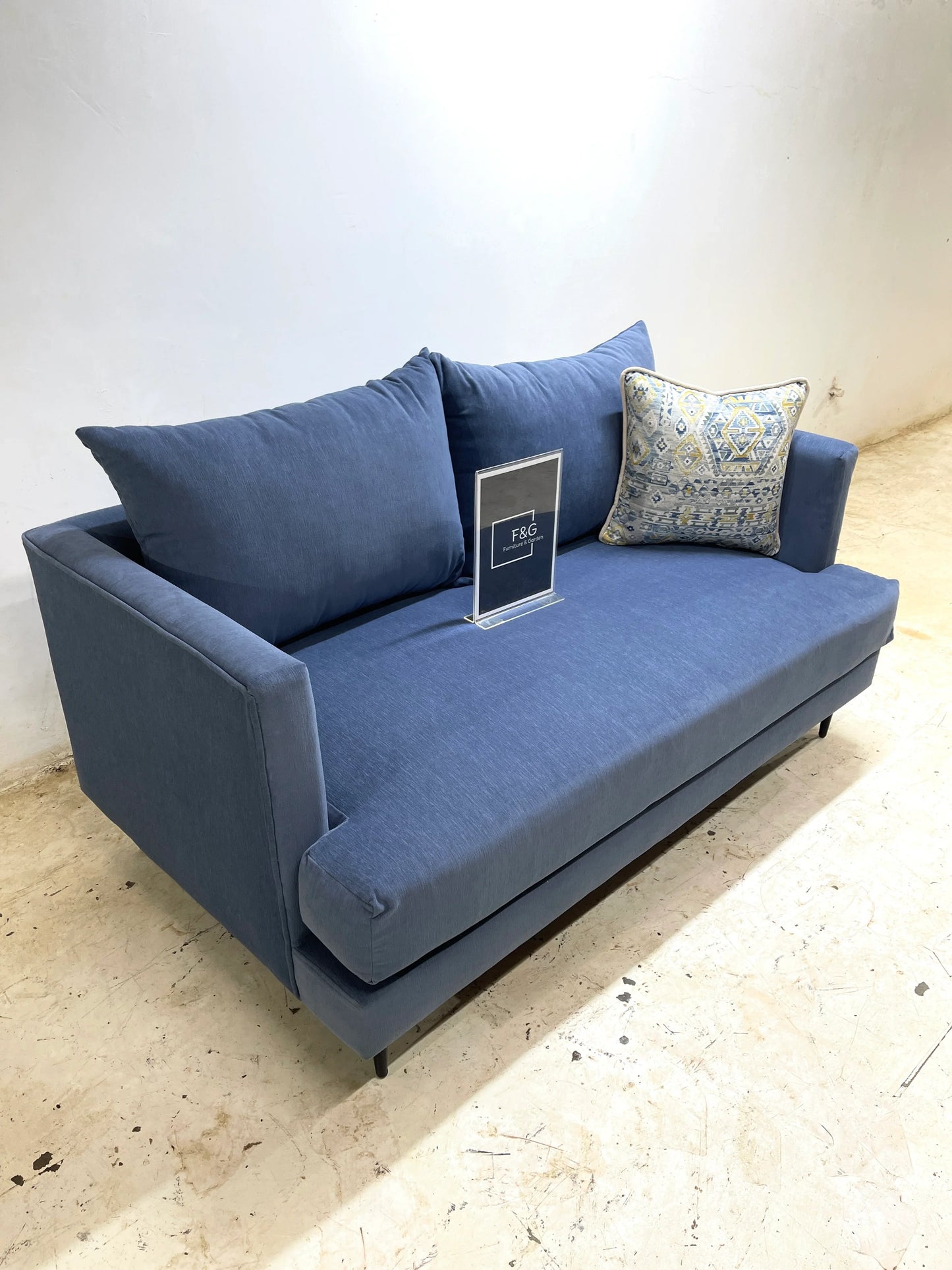 Modern blue fabric sofa with patterned cushion on concrete floor in minimalist room