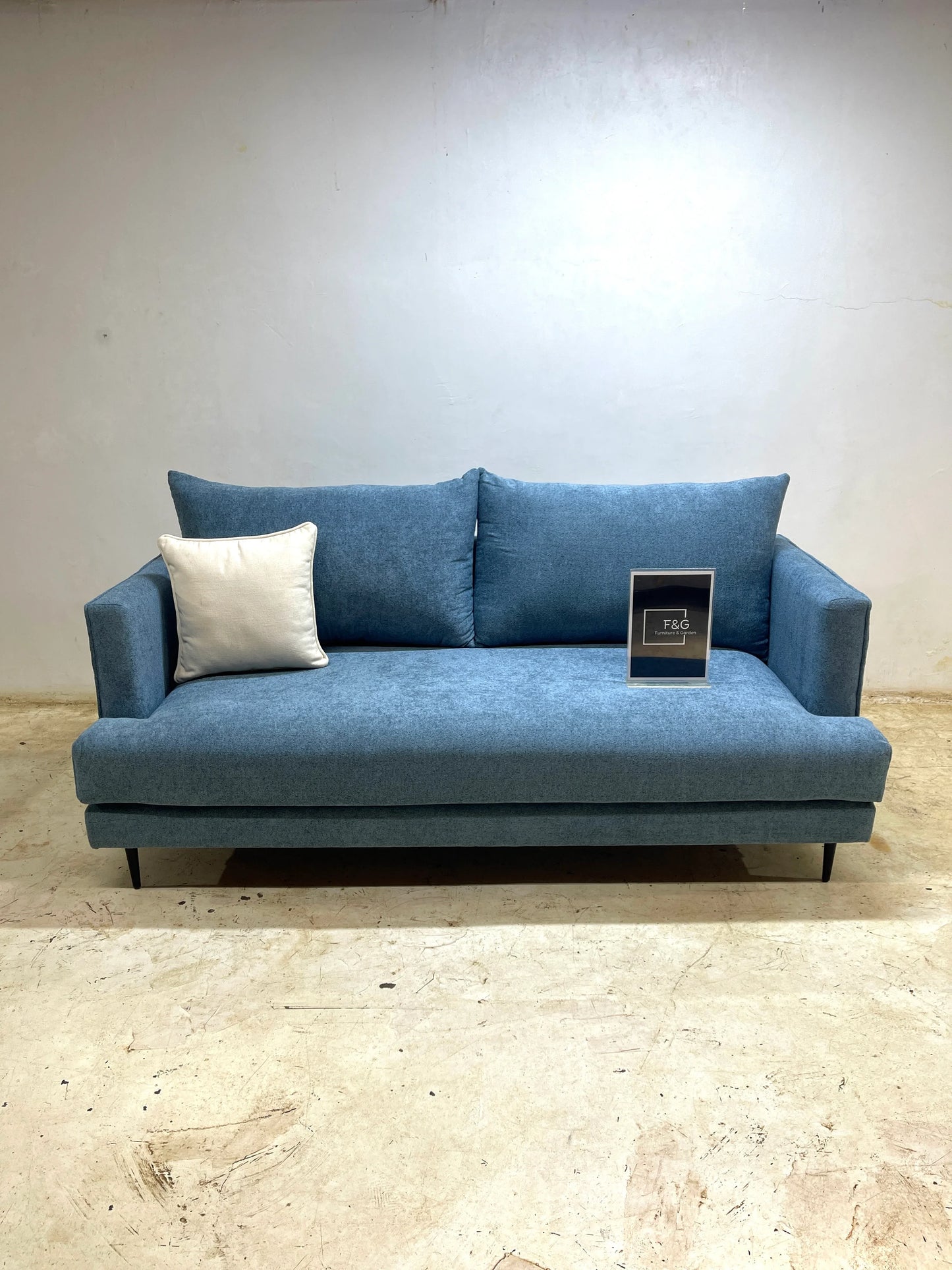 Modern blue fabric sofa with two back cushions and one cream throw pillow on a beige floor