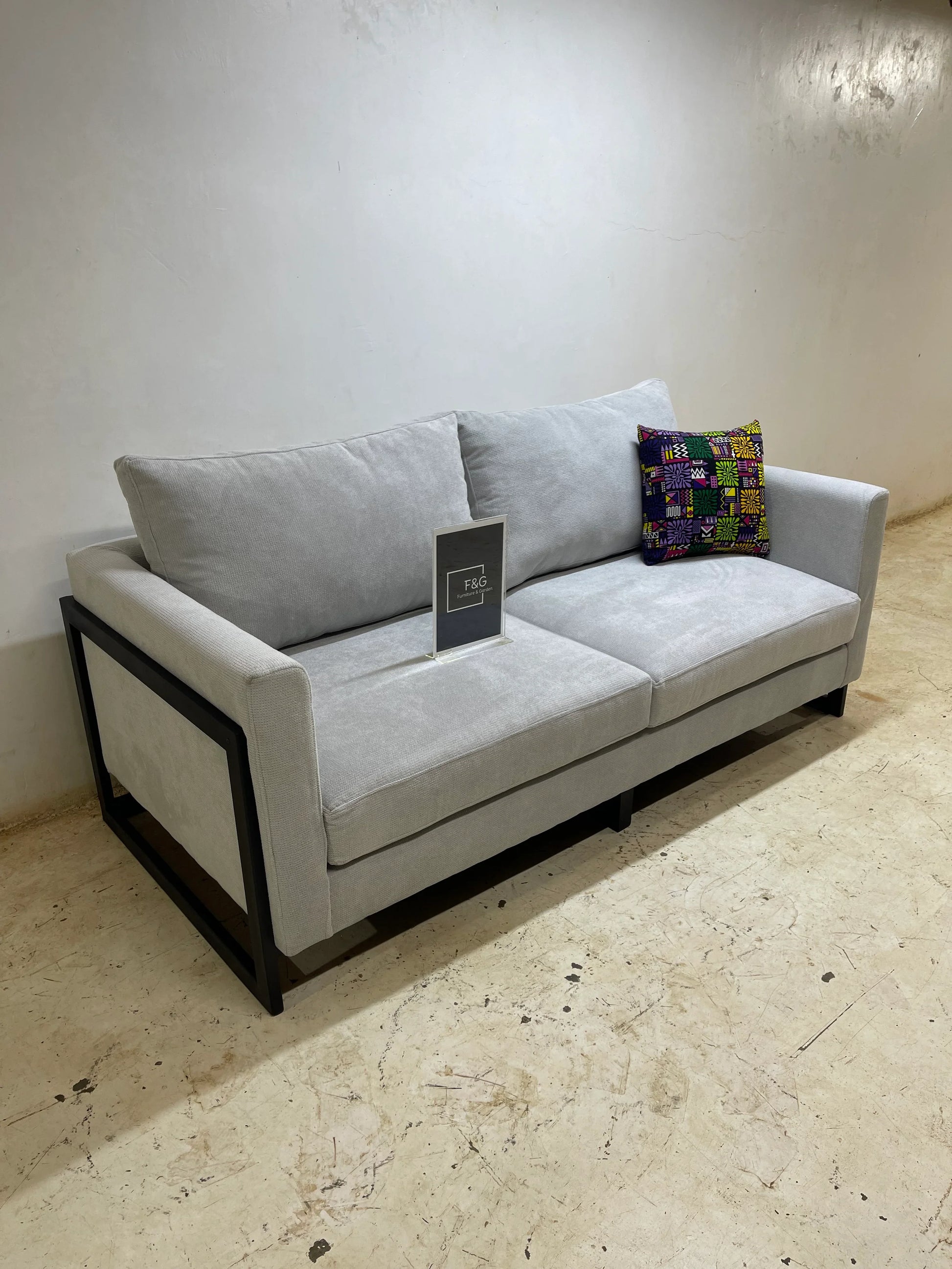 Modern light gray fabric sofa with black metal frame, colorful patterned throw pillow, on concrete floor
