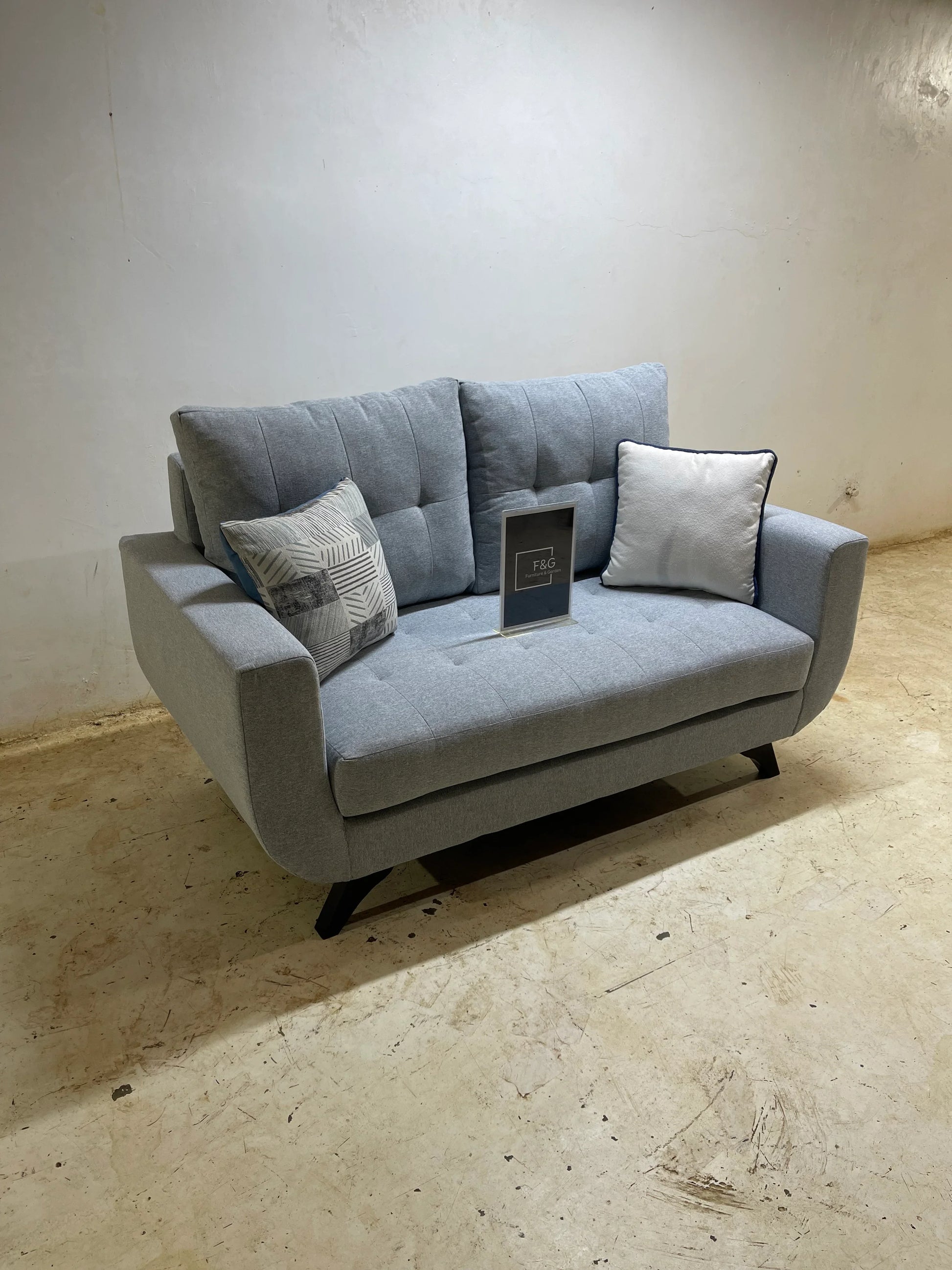 modern grey loveseat with two decorative pillows and F&G furniture sign on seat in simple room