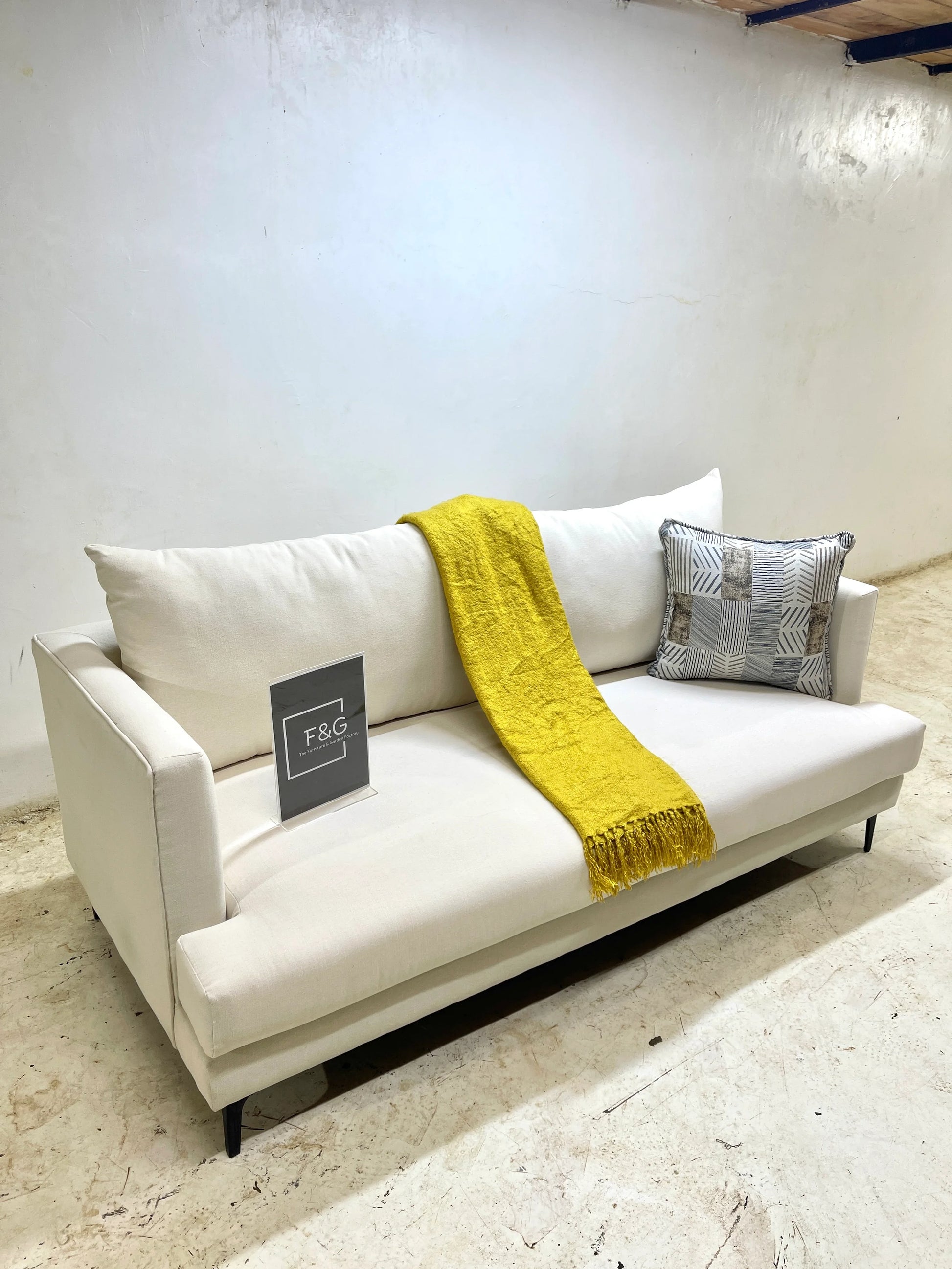Modern white fabric sofa with black legs, mustard yellow throw, and patterned cushion in minimal room