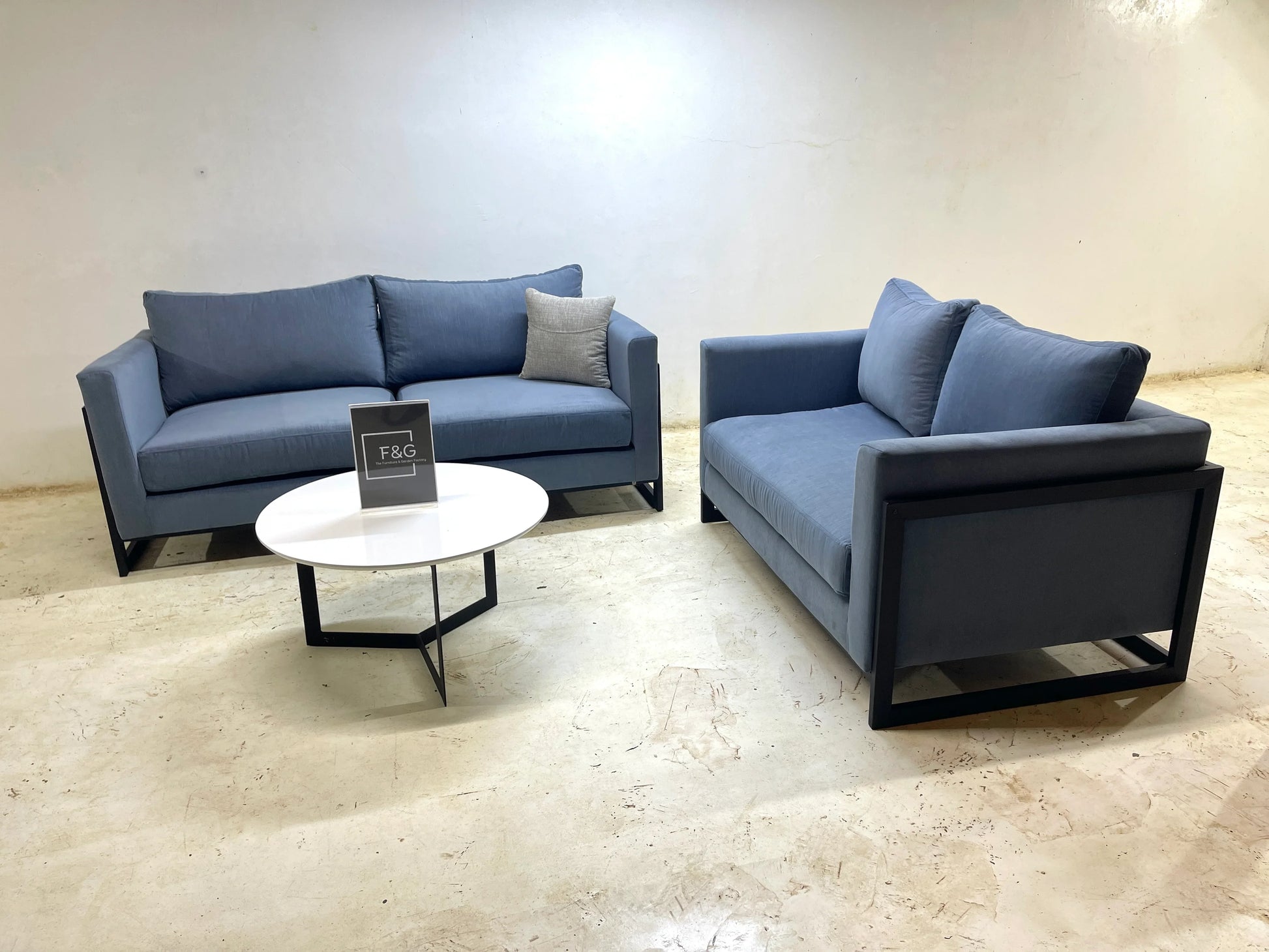 Modern living room setup with two blue fabric sofas and a round white coffee table on concrete floor