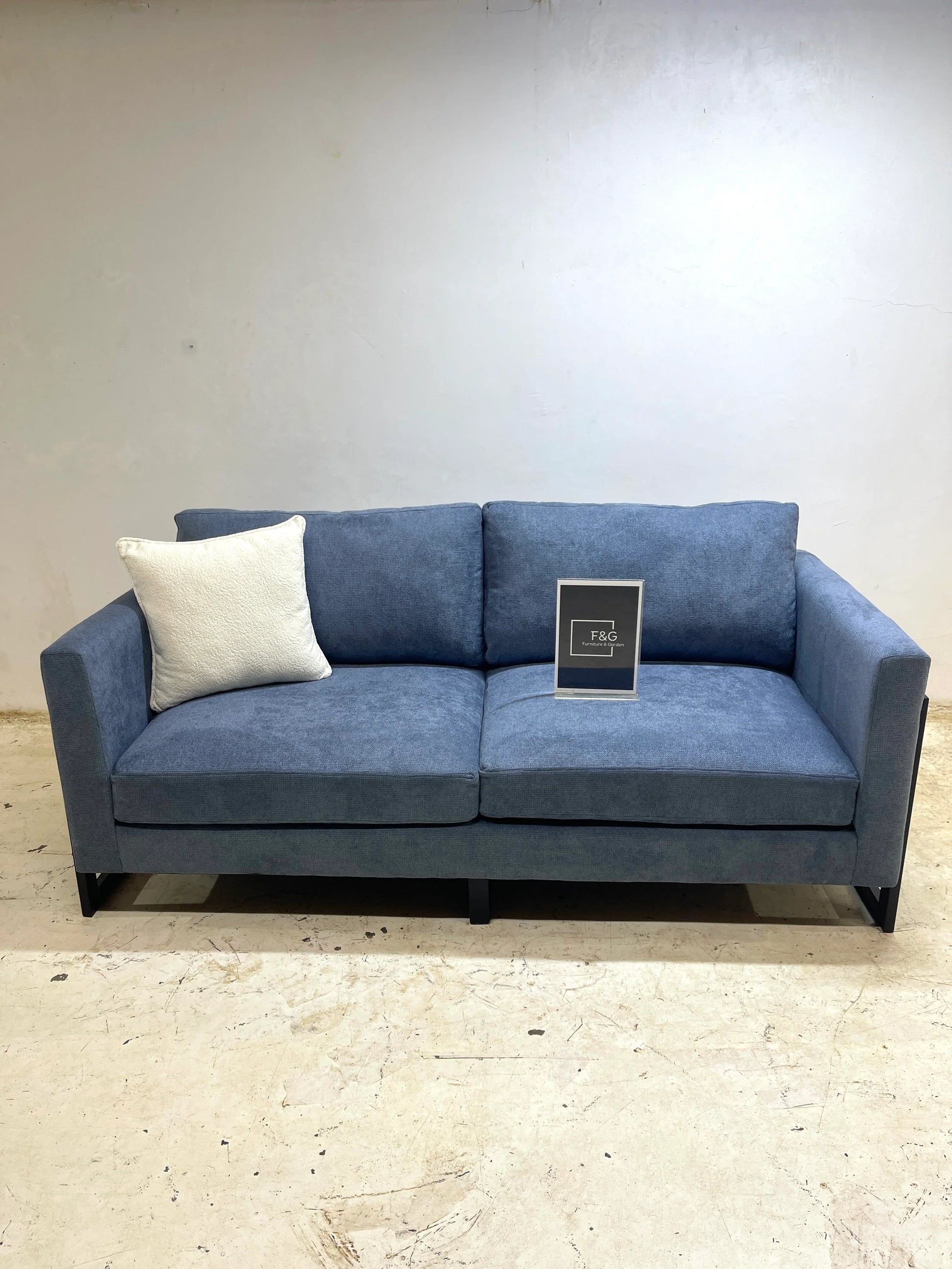 Modern blue fabric sofa with black metal legs, white cushion, and F&G Furniture & Garden sign