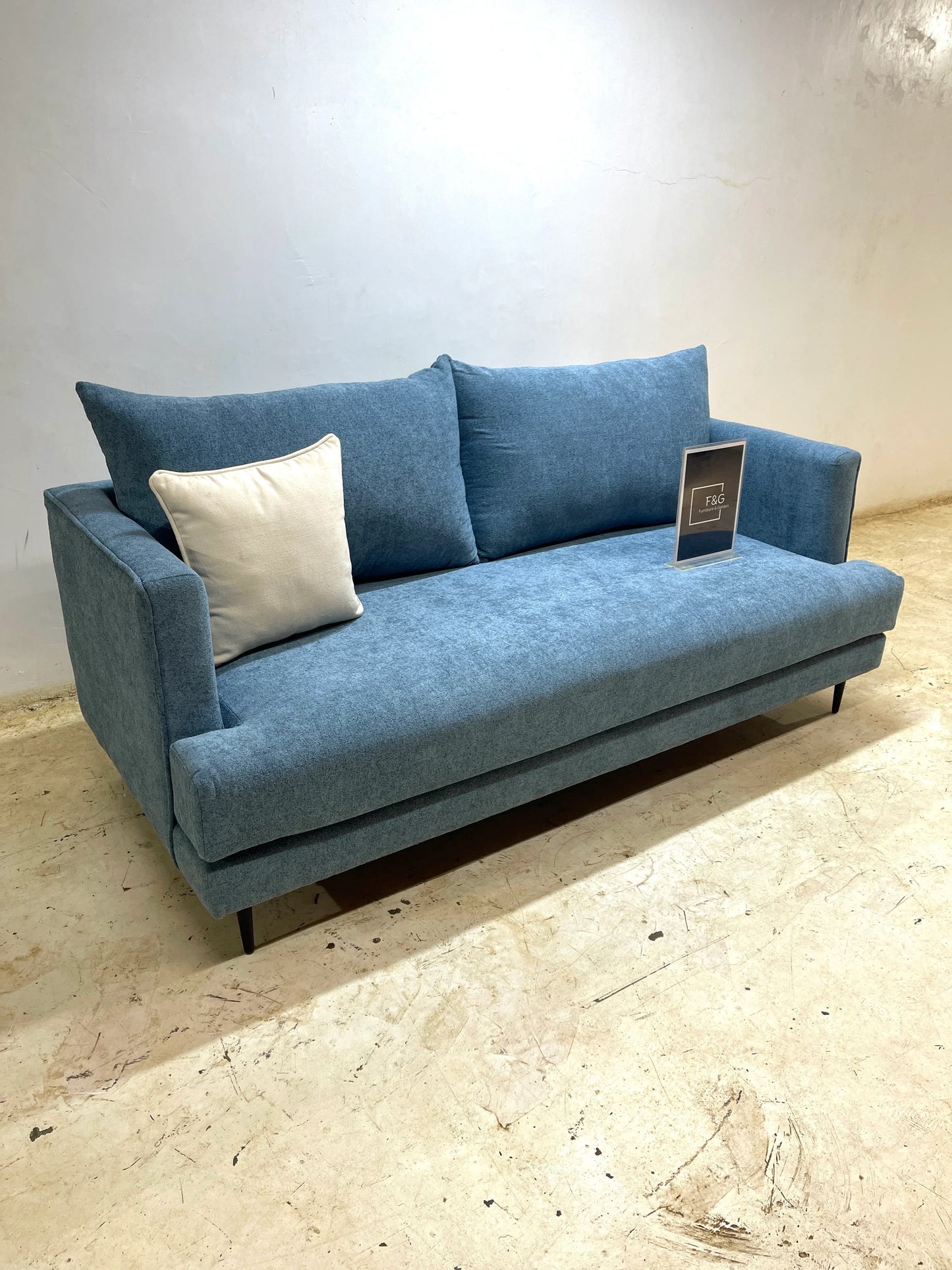 Modern blue fabric sofa with two cushions, including one white, in minimalist room with beige floor