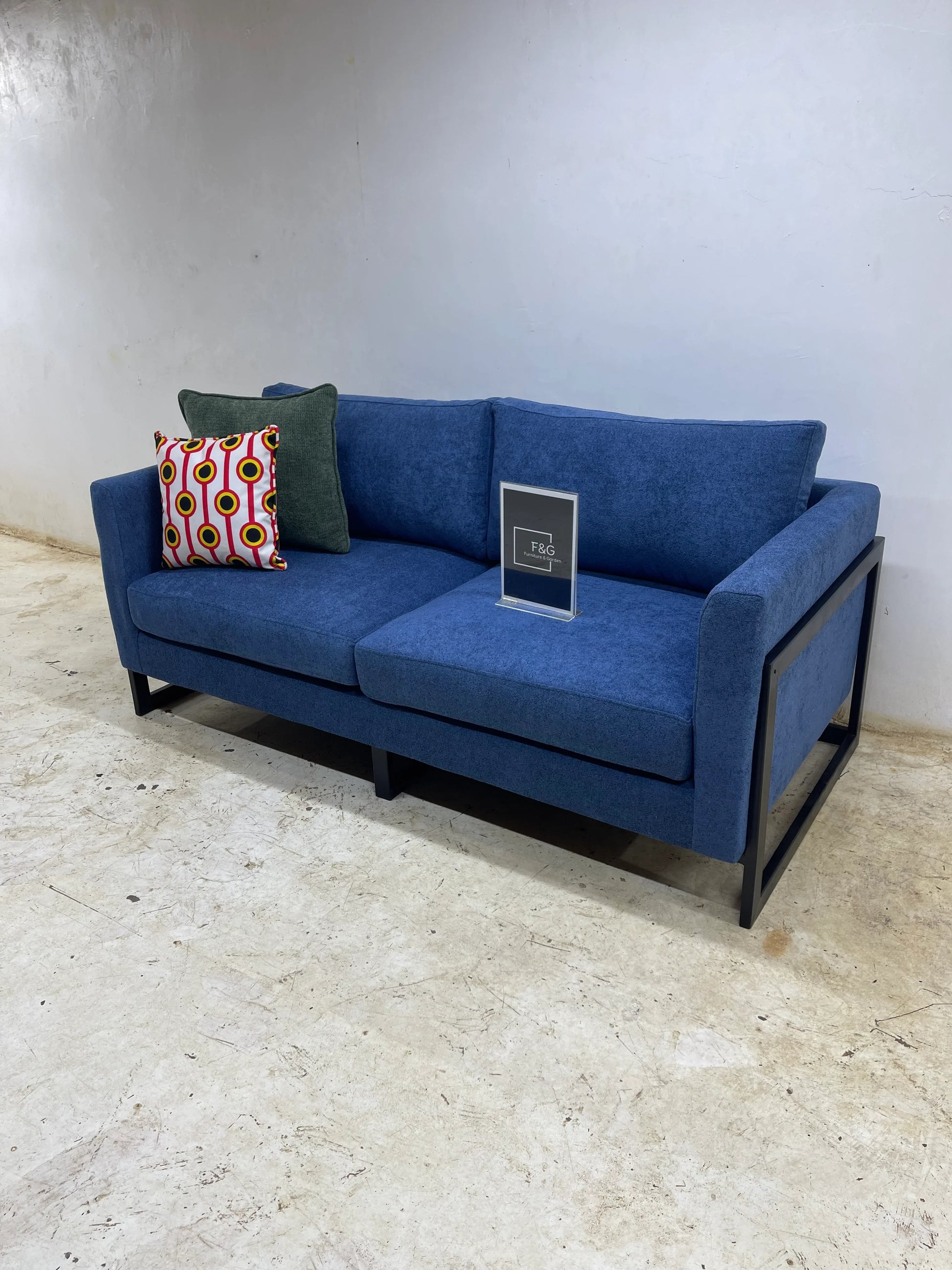 Modern blue fabric sofa with black metal frame, decorated with two throw pillows, set on textured floor