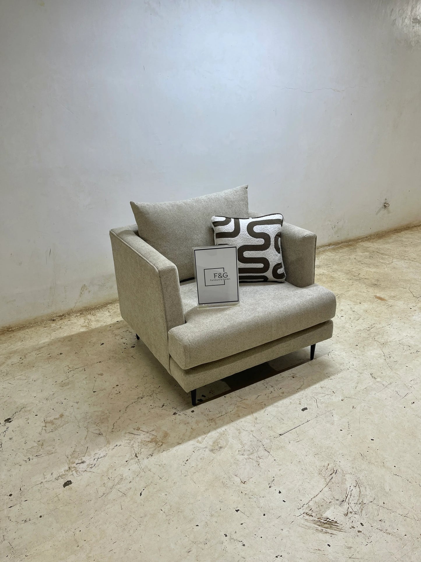 Modern beige armchair with patterned pillow and F&G Furniture & Garden sign on concrete floor