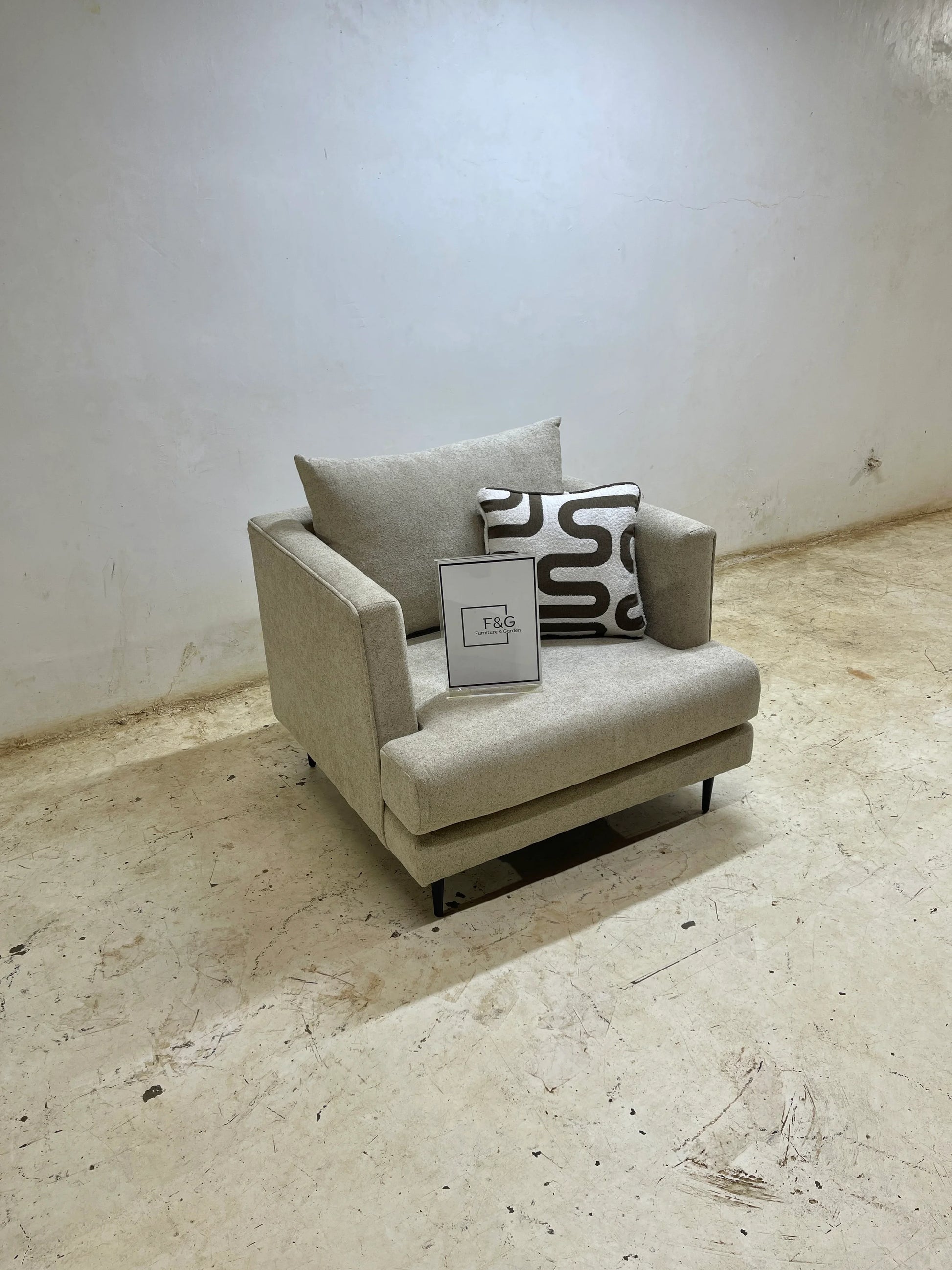Modern beige armchair with patterned pillow and F&G Furniture & Garden sign on concrete floor